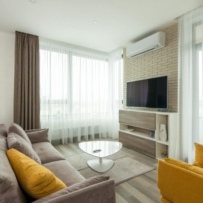 Spacious, modern living room with natural light, featuring a sofa, armchair, and a flat screen TV.